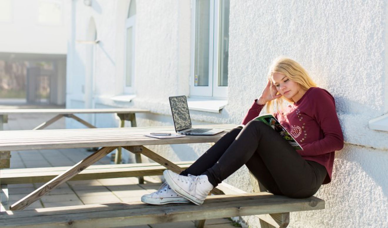 Ung jente sitter på benk og leser.
