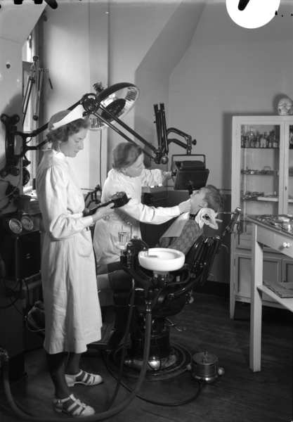 03 Foto: Teigens Fotoatelier/ DEXTRA Photo, Teknisk museum. Bildetekst Et barn sitter i tannlegestolen hos skoletannlegen ved Hersleb skole. Kvinnelig tannlege og tannlegeassistent. .I fotografens arkiv står det: Skoletannlege, Hersleb skole, Dr. Gytfe
