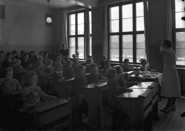 10 Foto: Teigens Fotoatelier/ DEXTRA Photo, Teknisk museum. Bildetekst: En kvinne i hvit kjortel, kanskje helsesøster eller tannleg, står ved et kateter i et klasserom og Demonstrerer hvordan man pusser tennene