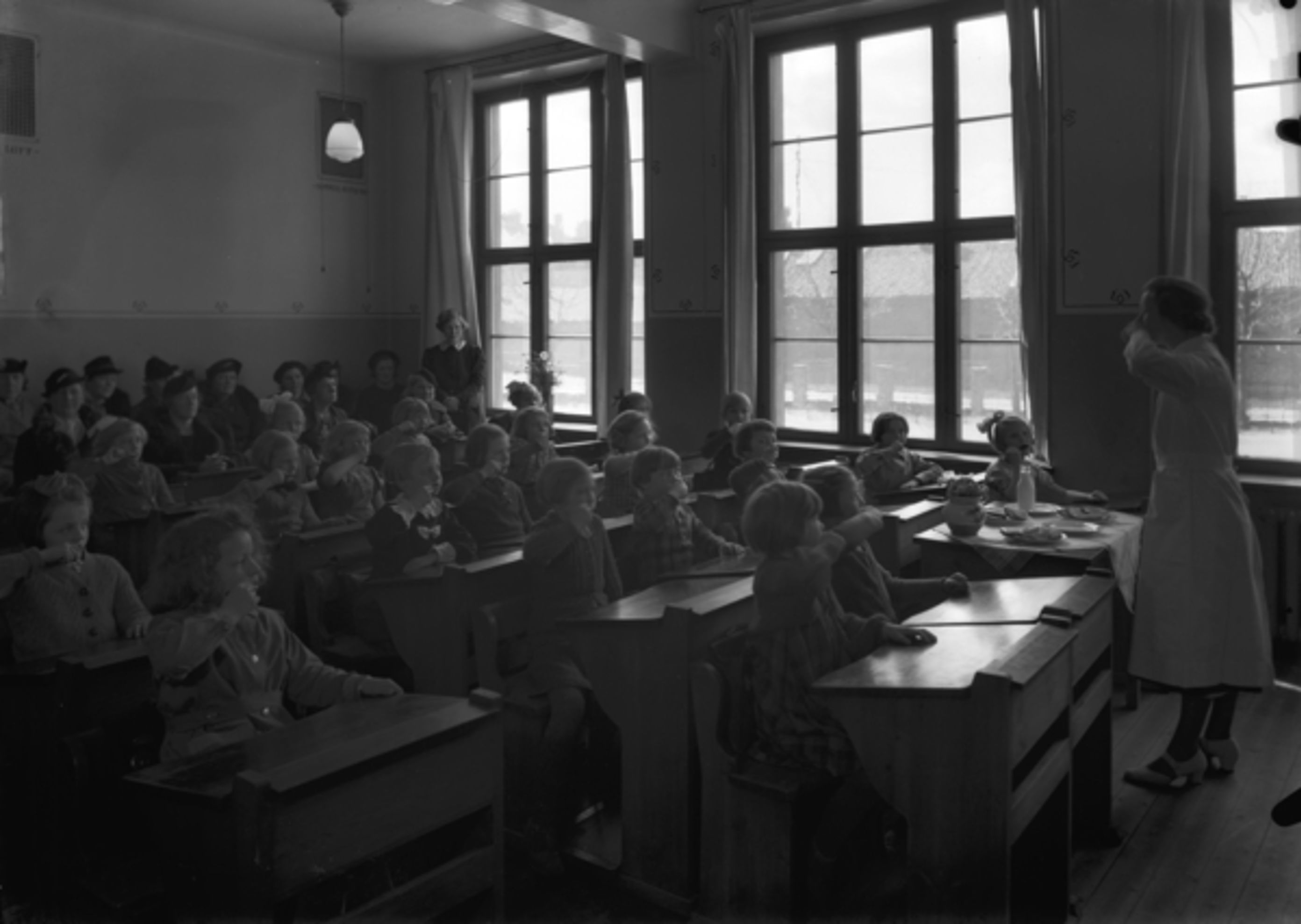 10 Foto: Teigens Fotoatelier/ DEXTRA Photo, Teknisk museum. Bildetekst: En kvinne i hvit kjortel, kanskje helsesøster eller tannleg, står ved et kateter i et klasserom og Demonstrerer hvordan man pusser tennene