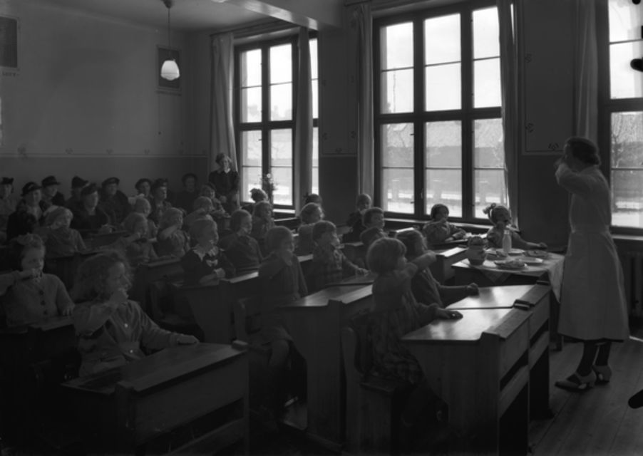 10 Foto: Teigens Fotoatelier/ DEXTRA Photo, Teknisk museum. Bildetekst: En kvinne i hvit kjortel, kanskje helsesøster eller tannleg, står ved et kateter i et klasserom og Demonstrerer hvordan man pusser tennene